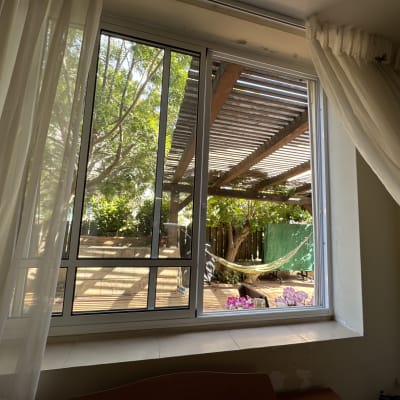 חלון עם תריסים פתוחים, וילונות לבנים בצדדים