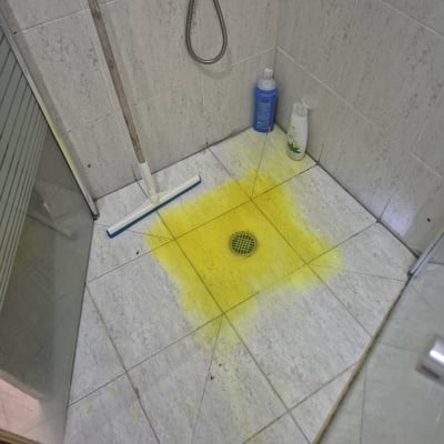 רצפת מקלחת עם כתם צהוב, מגב ובקבוקי ניקוי