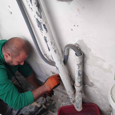 אדם עם כפפות מתקן צינור ליד קיר מתקלף