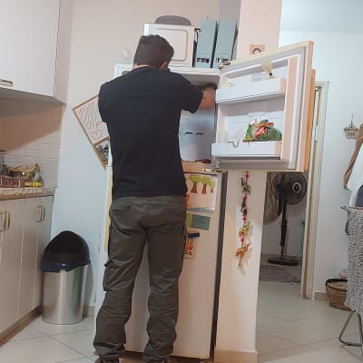 אדם מתקן מקרר עם דלת פתוחה וכלי עבודה