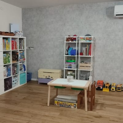 חדר ילדים עם מדפים מלאים במשחקים וספרים, שולחן קטן וצעצועים על הרצפה.