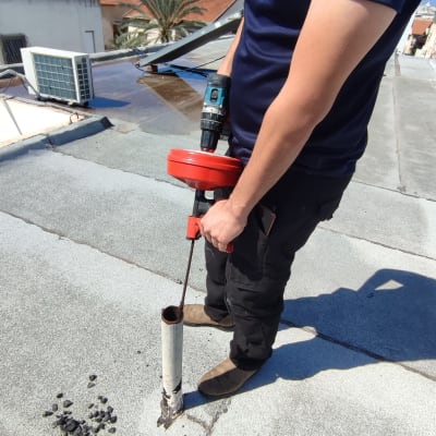 אדם משתמש במקדחה לפתיחת צינור על גג