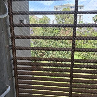 רשת מתכת על חלון עם נוף לעצים ובניינים