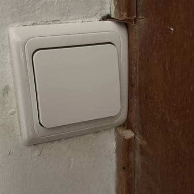 מתג חשמל לבן על קיר ליד דלת עץ