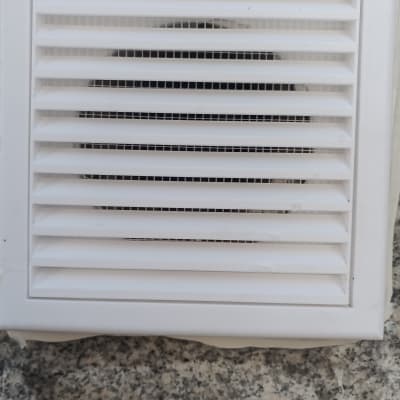 פתח אוורור לבן עם תריסים על קיר בטון