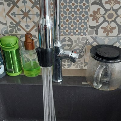 ברז מים זורמים בכיור מטבח עם רקע אריחים מעוצבים