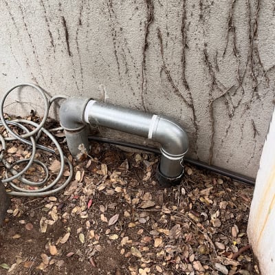 צינור מתכת ליד קיר עם עלים יבשים על הקרקע