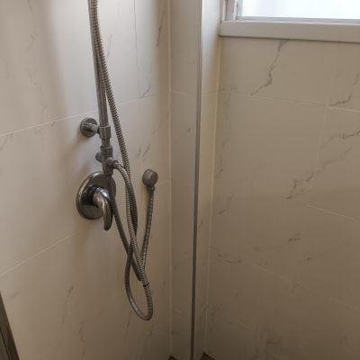 ראש מקלחת עם צינור מתכת על קיר אריחים