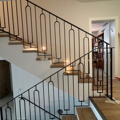 מעקה מתכת שחור עם עיצוב גיאומטרי על מדרגות עץ