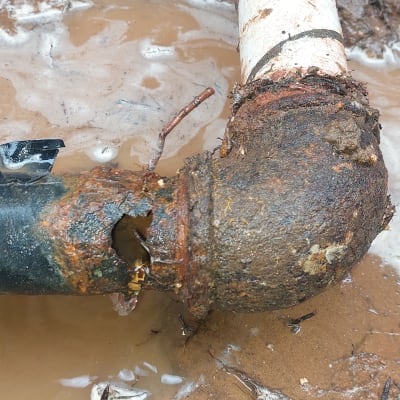 צינור חלוד עם חור ודליפת מים באדמה רטובה