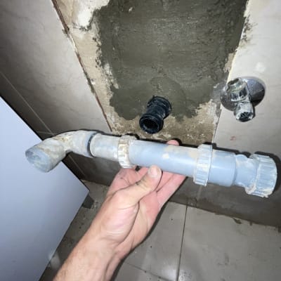 יד מחזיקה צינור ליד קיר עם חור ותשתית אינסטלציה