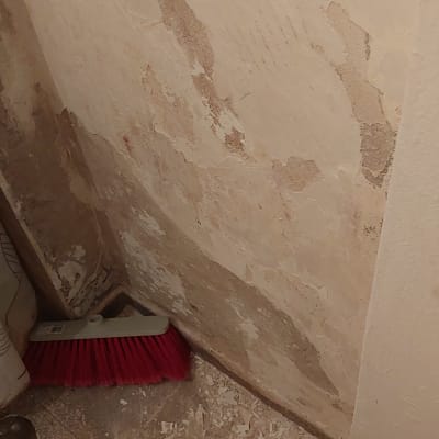 קיר מתקלף עם מטאטא וחתיכות צבע על הרצפה