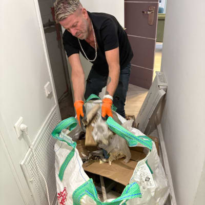 אדם עם כפפות כתומות מפנה שקית פסולת במסדרון