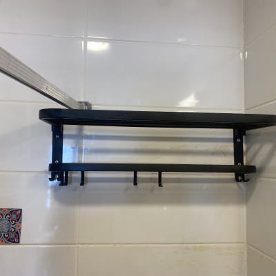 מדף מתכת שחור עם ווים על קיר אריחים לבנים