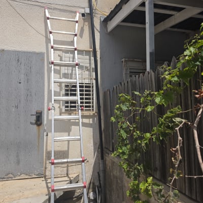 סולם ליד קיר חיצוני עם צינור וגדר עץ