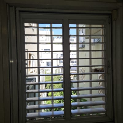 תריסים לבנים על חלון עם נוף עירוני