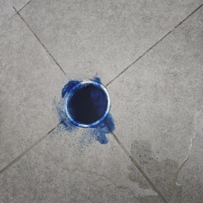 ניקוז עם סימני צבע כחול על רצפה אפורה