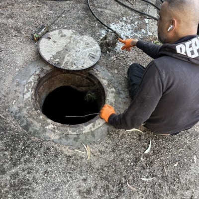 אדם עם כפפות כתומות ליד פתח ביוב פתוח