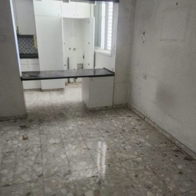 חדר ריק עם רצפת שיש ומטבח קטן ברקע