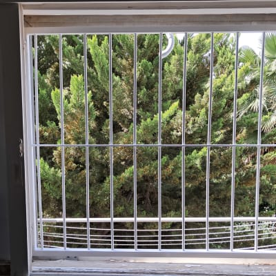 סורגי חלון לבנים עם נוף עצים ירוקים