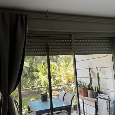 תריסים סגורים על חלון עם וילונות וצמחים במרפסת