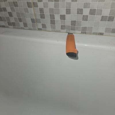 ידית כתומה על אמבטיה עם אריחים אפורים