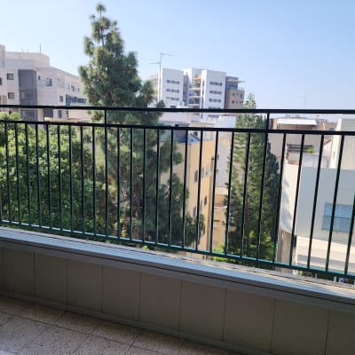 מעקה מתכת ירוק במרפסת עם נוף עירוני ועצים