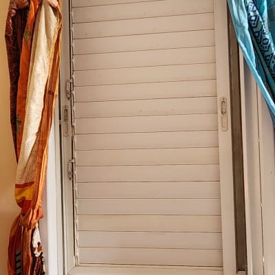 תריסים לבנים סגורים בחלון עם וילונות צבעוניים בצדדים