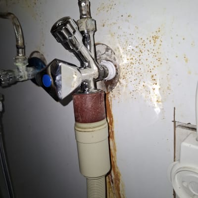 ברז מתכת עם צינור גמיש וחלודה על הקיר