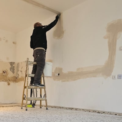 אדם על סולם מבצע תיקוני קיר בחדר
