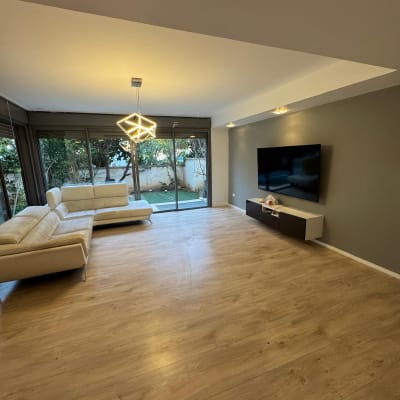 חדר מגורים עם רצפת עץ, ספה וטלוויזיה על הקיר