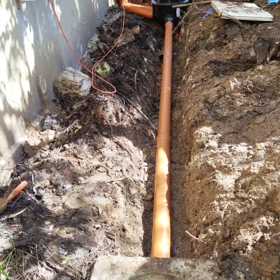 צינור כתום מונח בתעלה ליד קיר בניין