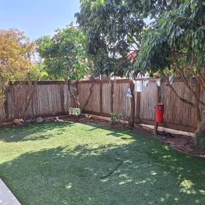 חצר עם דשא מלאכותי ועצים לאורך הגדר