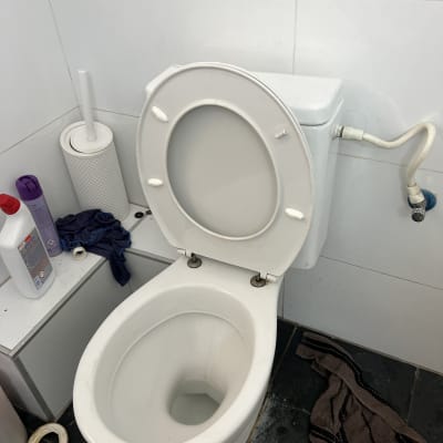 אסלה עם חיבורי צנרת וכלי ניקוי בחדר אמבטיה