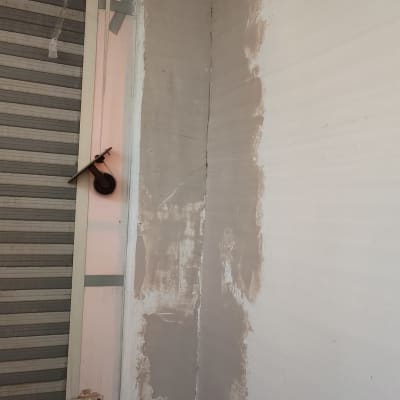 קיר עם תיקוני טיח ליד חלון עם תריסים