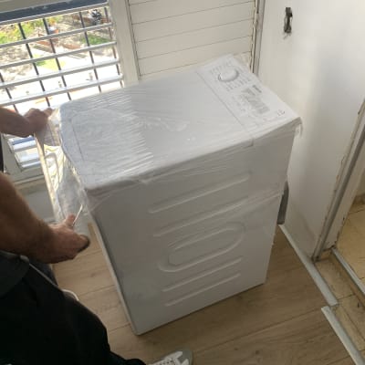 אדם מסיר עטיפה ממכונת כביסה חדשה