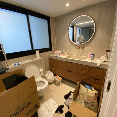 חדר אמבטיה עם קופסאות קרטון, שקיות וכביסה על הרצפה.