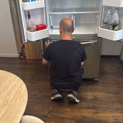 אדם מתקן מקרר פתוח במטבח עם כלים