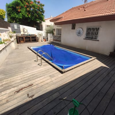 בריכה מכוסה בכיסוי כחול על דק עץ בגינה