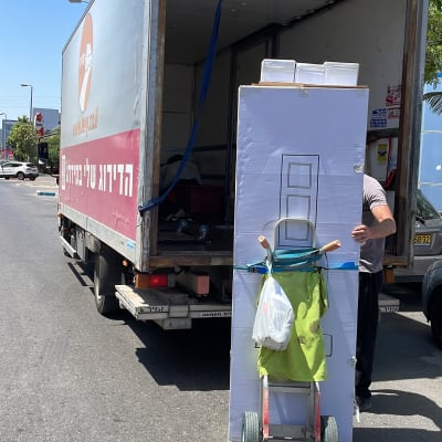 אדם מעביר קרטון גדול עם עגלה למשאית פתוחה