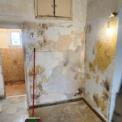 קירות מתקלפים, מטאטא על הרצפה, מנורה חשופה