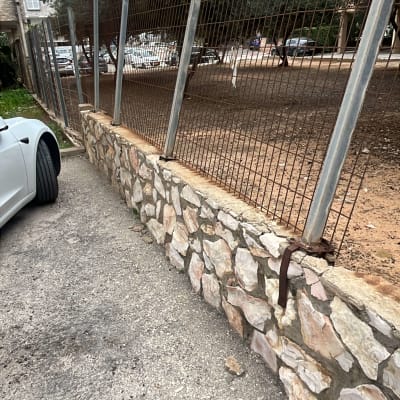 גדר מתכת על קיר אבן ליד רכב חונה