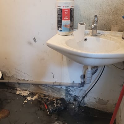 כיור עם צנרת גלויה וכלי עבודה על הרצפה