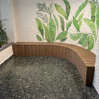 ספסל עץ מעוקל ליד קיר עם עלים ירוקים