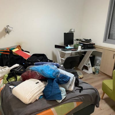 חדר מבולגן עם בגדים וחפצים על המיטה