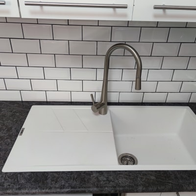 כיור מטבח עם ברז נירוסטה על רקע אריחים לבנים