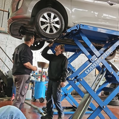 רכב על מעלית מוסך עם שני מכונאים בודקים