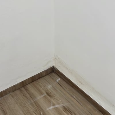 פינת חדר עם רצפת עץ וקיר עם סימני רטיבות