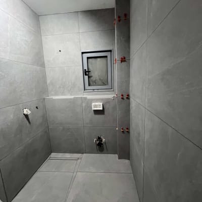 חדר אמבטיה עם אריחים אפורים, חלון קטן, חיבורים לצנרת