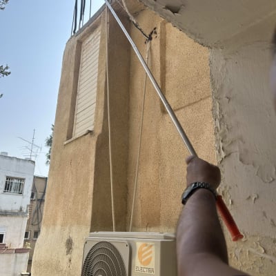 אדם מחזיק מוט ליד מזגן על קיר חיצוני